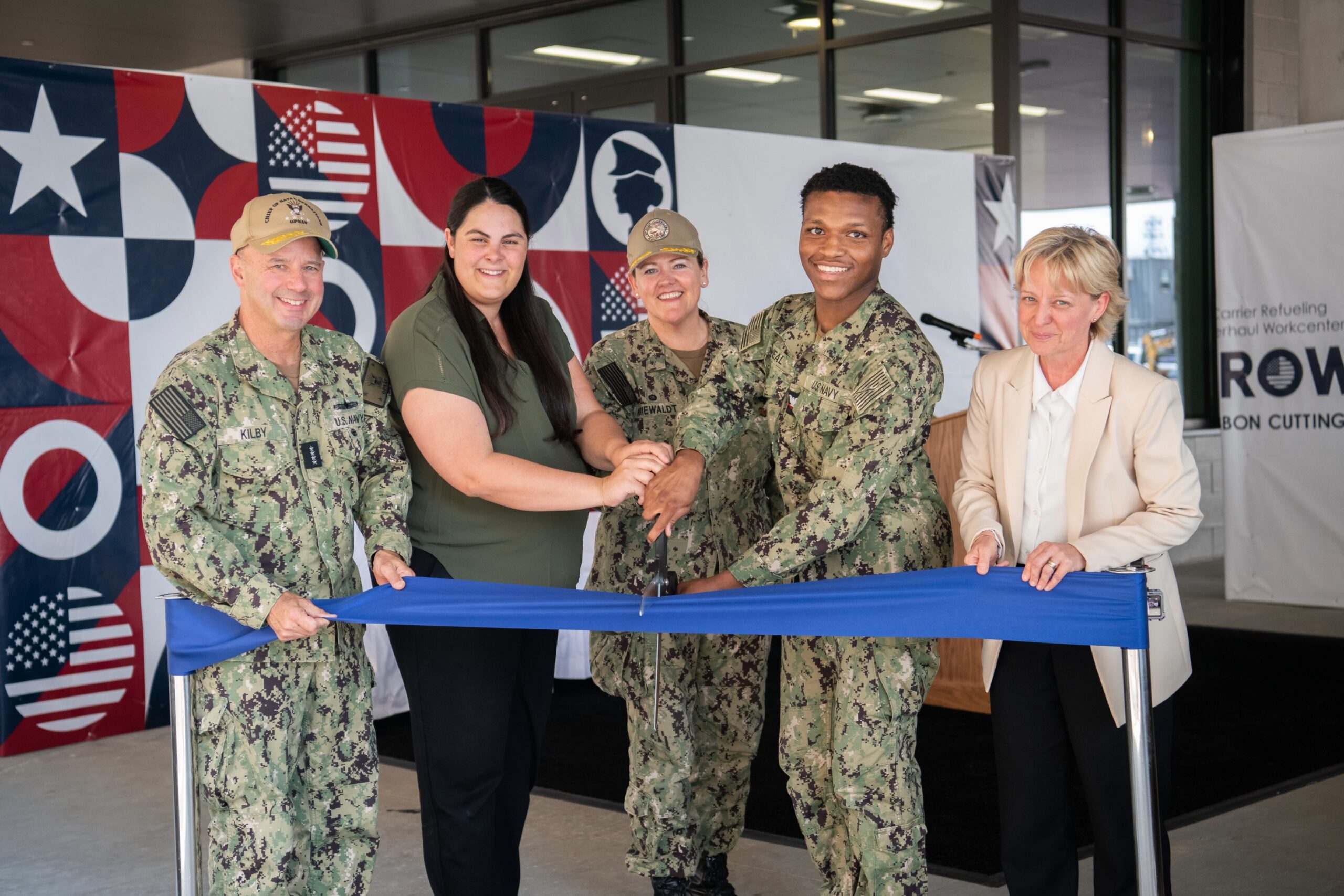 Five people (VCNO, HII-NNS employee, Ashley Martin, Capt Hannah Kriewaldt, EM3 Dashon McNeal, assigned to CVN 74 and Kari Wilkinson) cut the a blue ribbon to celebrate the opening of the Carrier Refueling Overhaul Workcenter.
